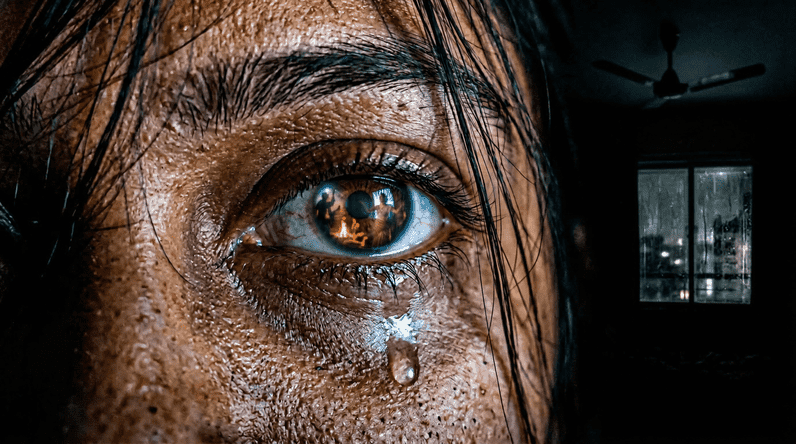 A pair of dark eyes reflecting the glow of a smartphone screen in complete darkness, a single tear on the cheek — the raw emotion of being lost in a Bengali web series at 2am